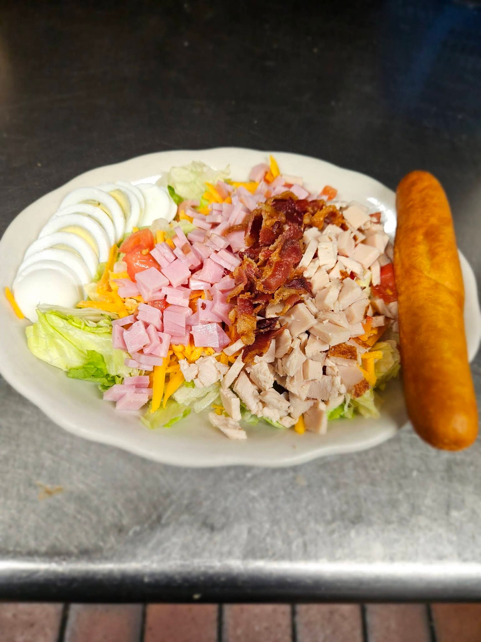 Chef salad with ham, turkey, bacon, egg, and a breadstick